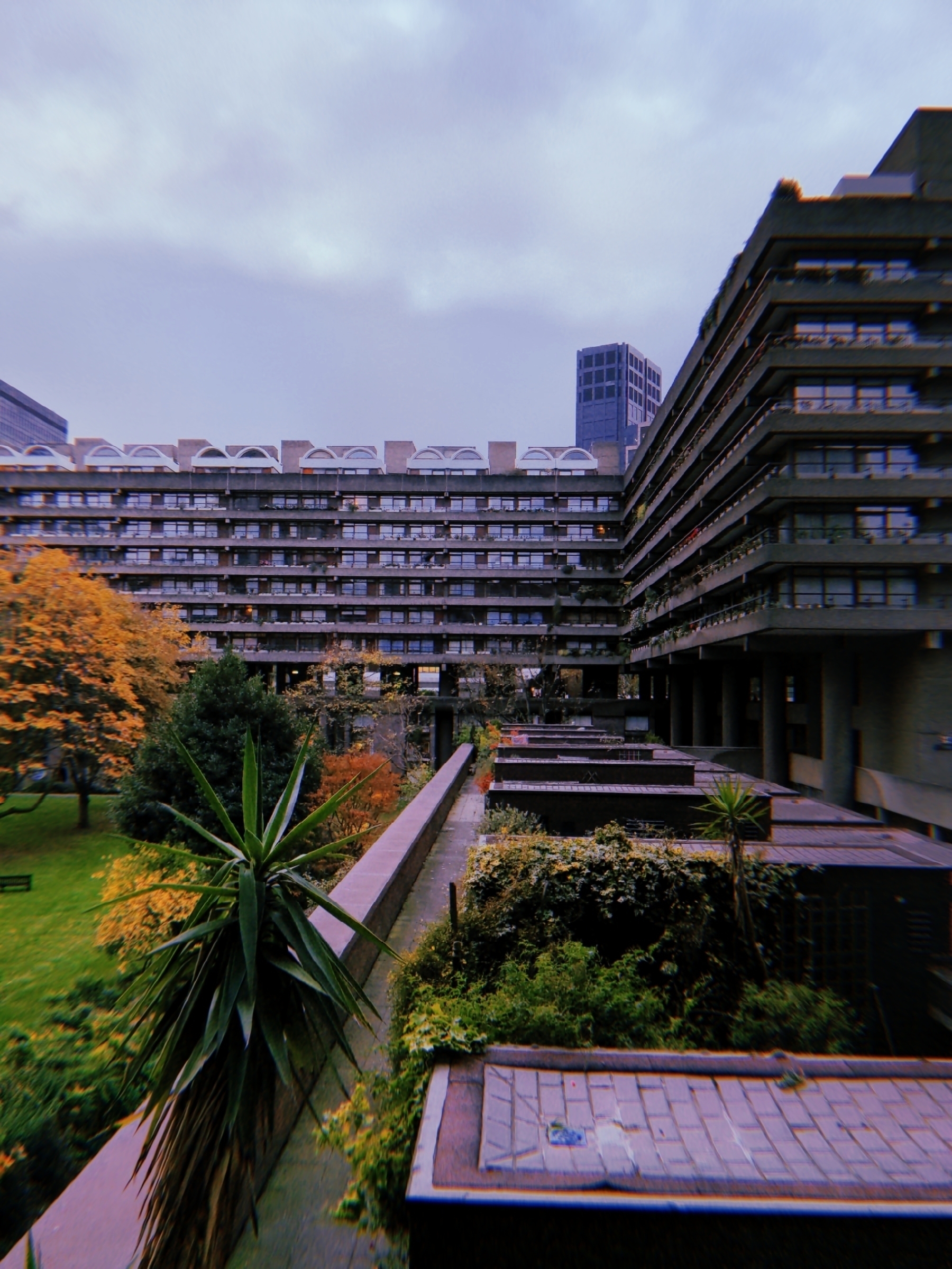 A modern architectural structure with multiple levels overlooks a lush green garden with trees and shrubs.