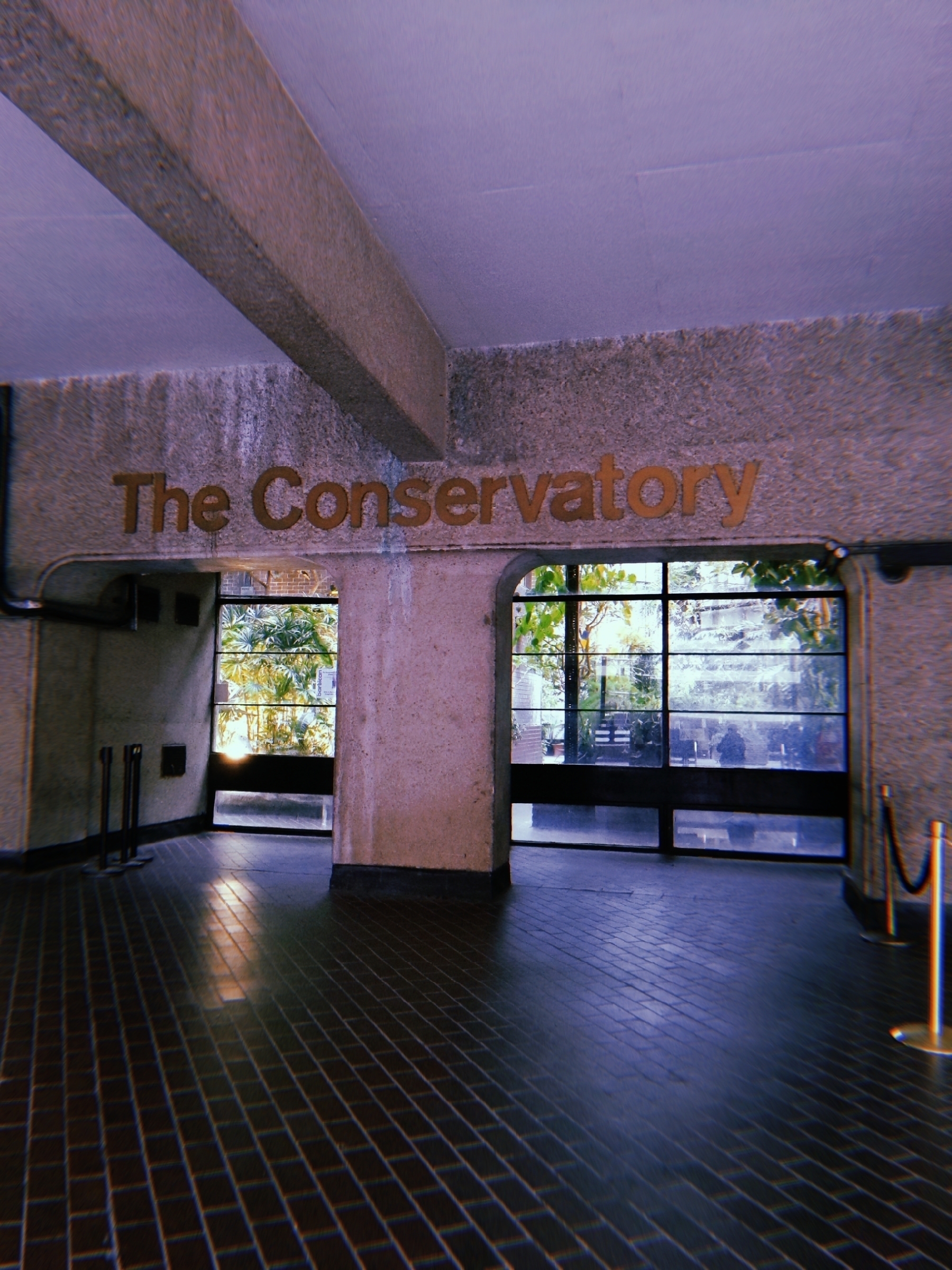 A room with textured walls features a sign reading "The Conservatory" above a set of windows overlooking a garden.