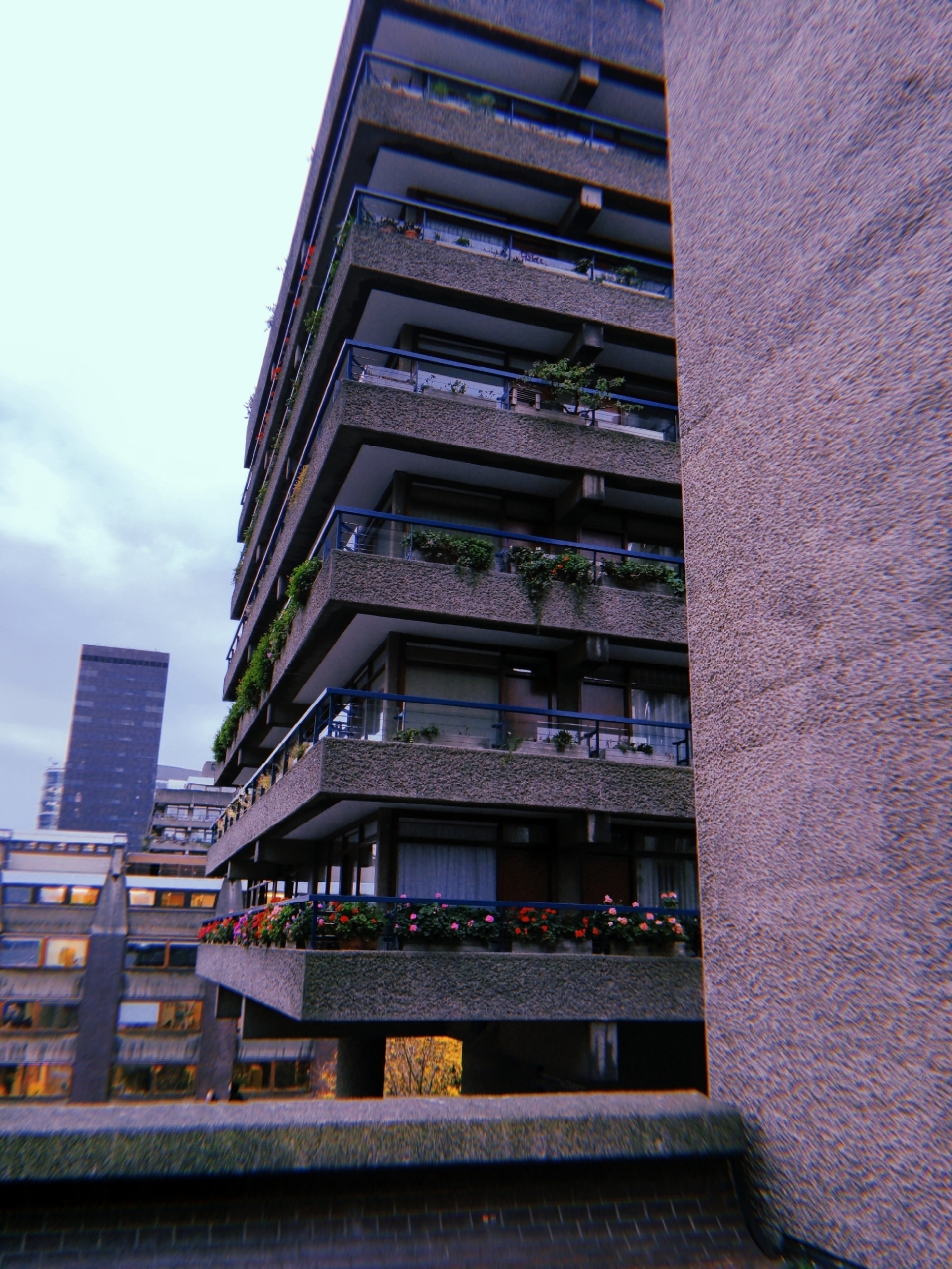 A brutalist-style building features staggered balconies adorned with plants and flowers.