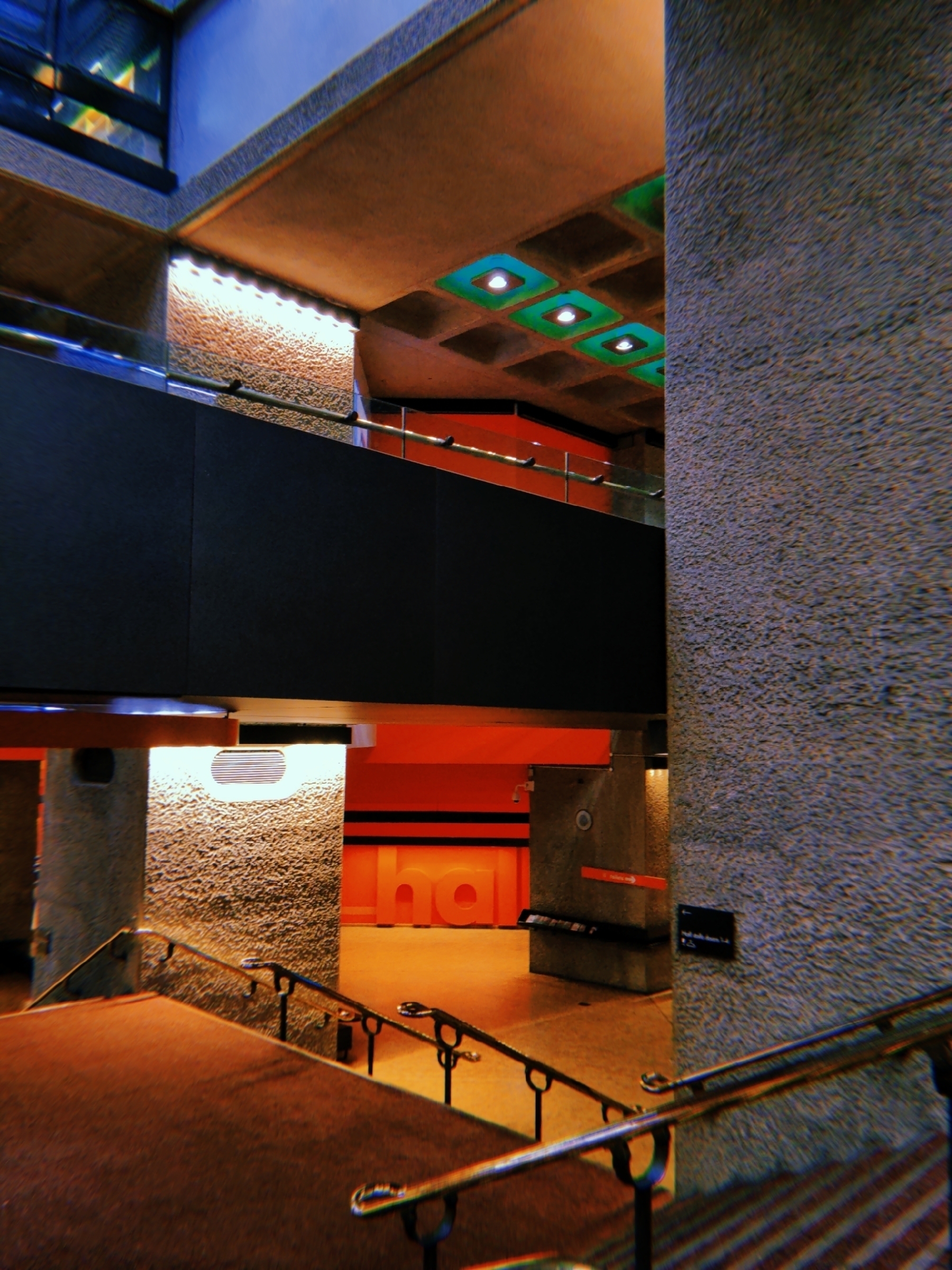 A modern interior space features textured concrete walls, vibrant orange accents, and a sleek staircase with metal railings.