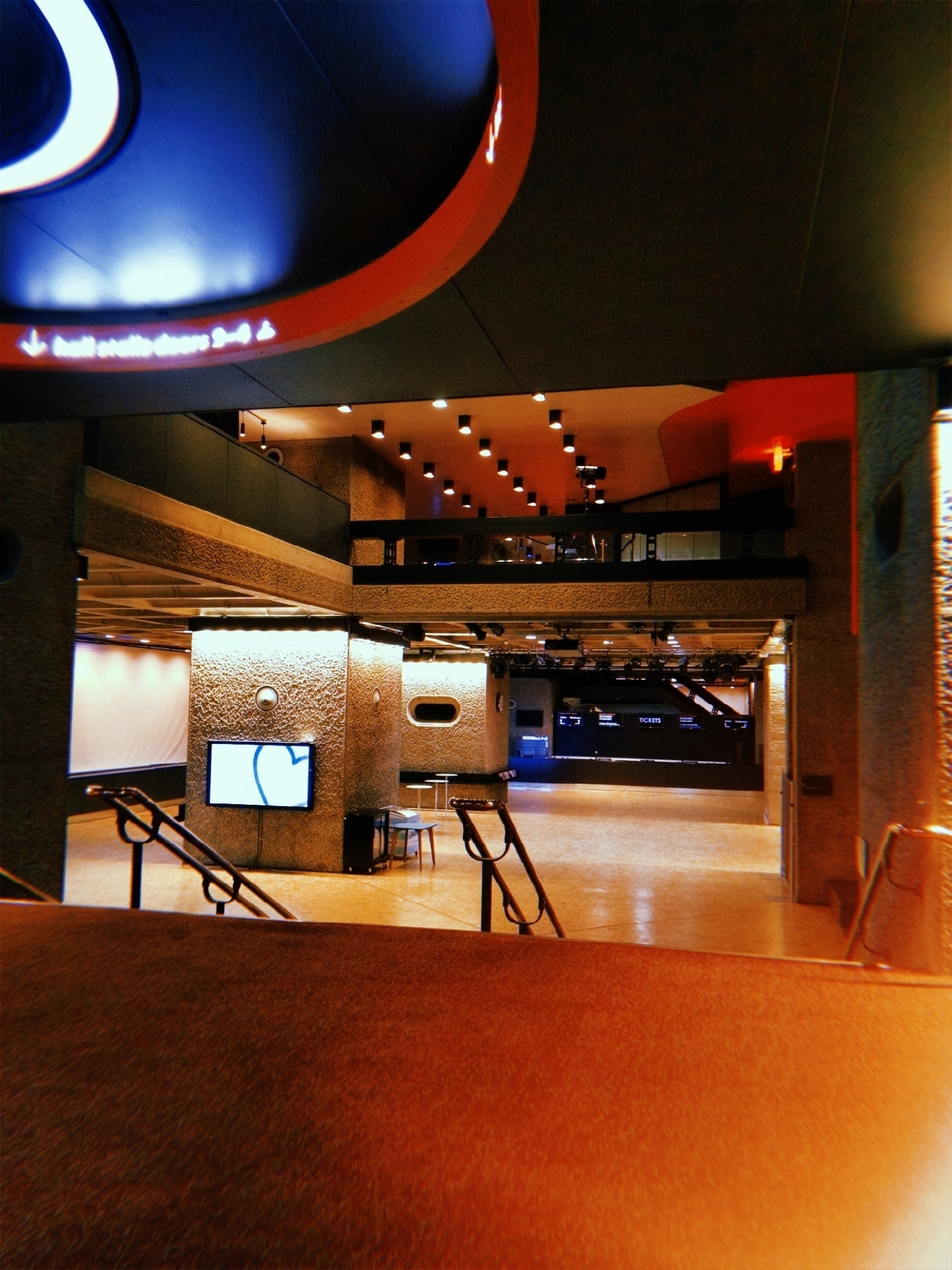 A modern interior space features a large open area with staircases, mood lighting, and digital screens.