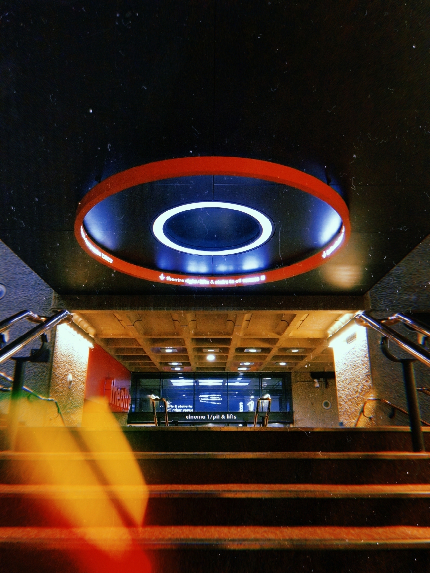 A futuristic circular light fixture illuminates a stairwell leading to an underground space with modern architectural elements.