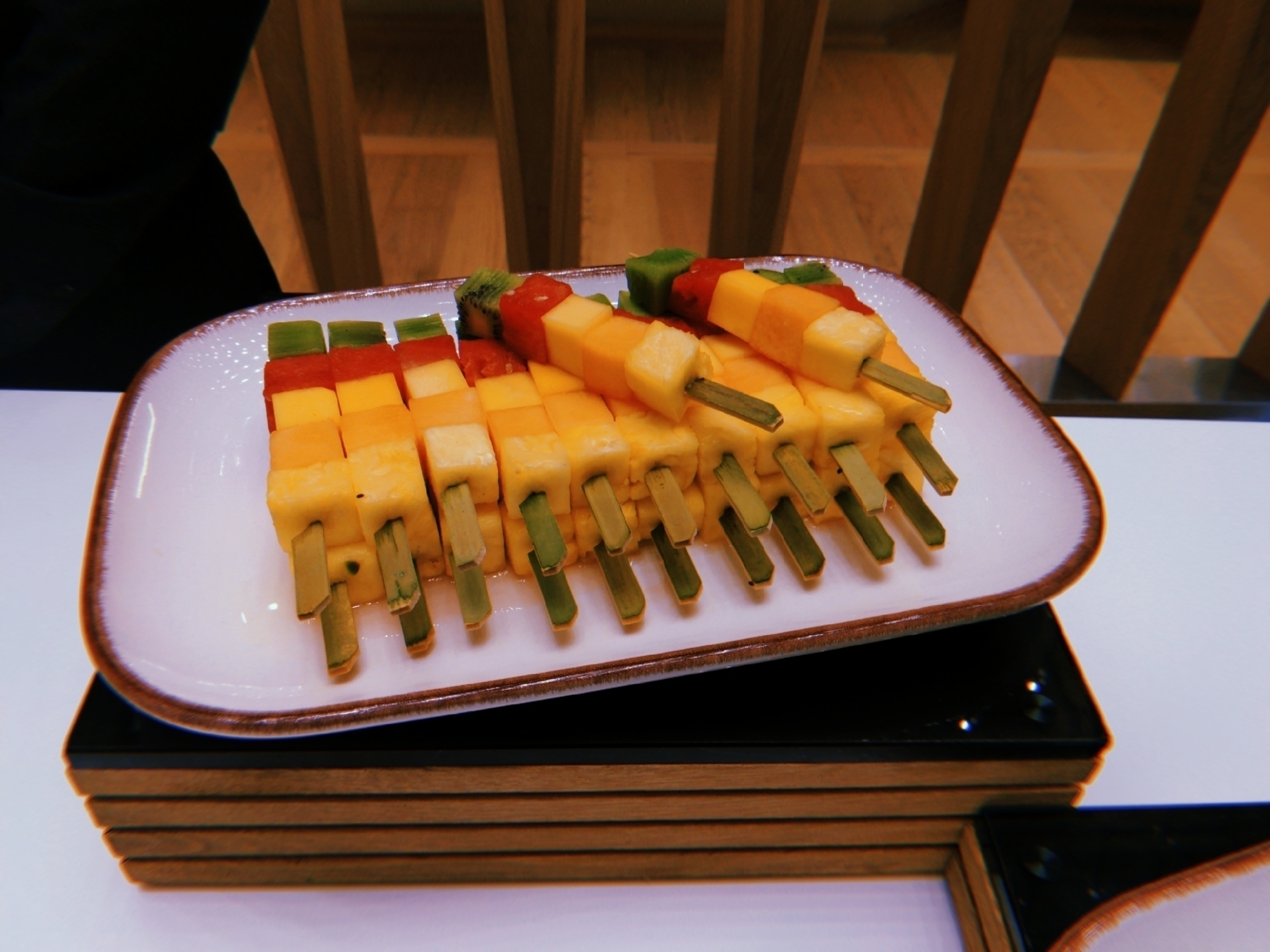 A plate of neatly arranged colorful fruit skewers with layers of different fruits is displayed.