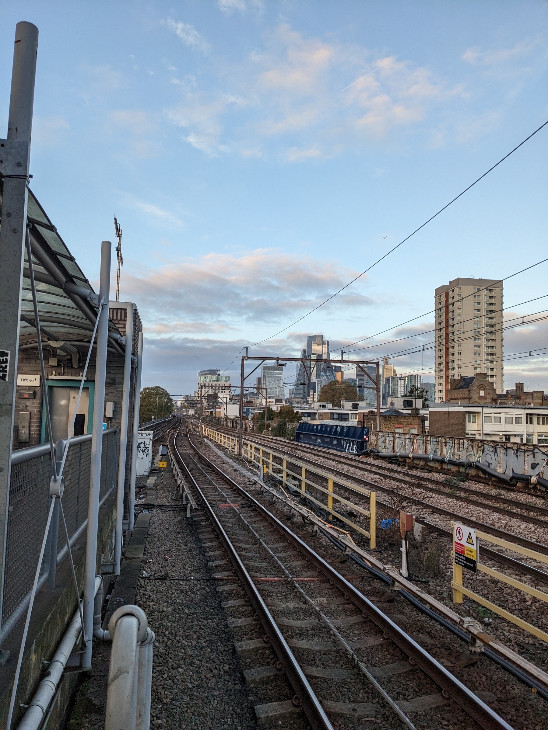 A London railway track stretches into the distance with urban buildings and a cloudy sky in the background.