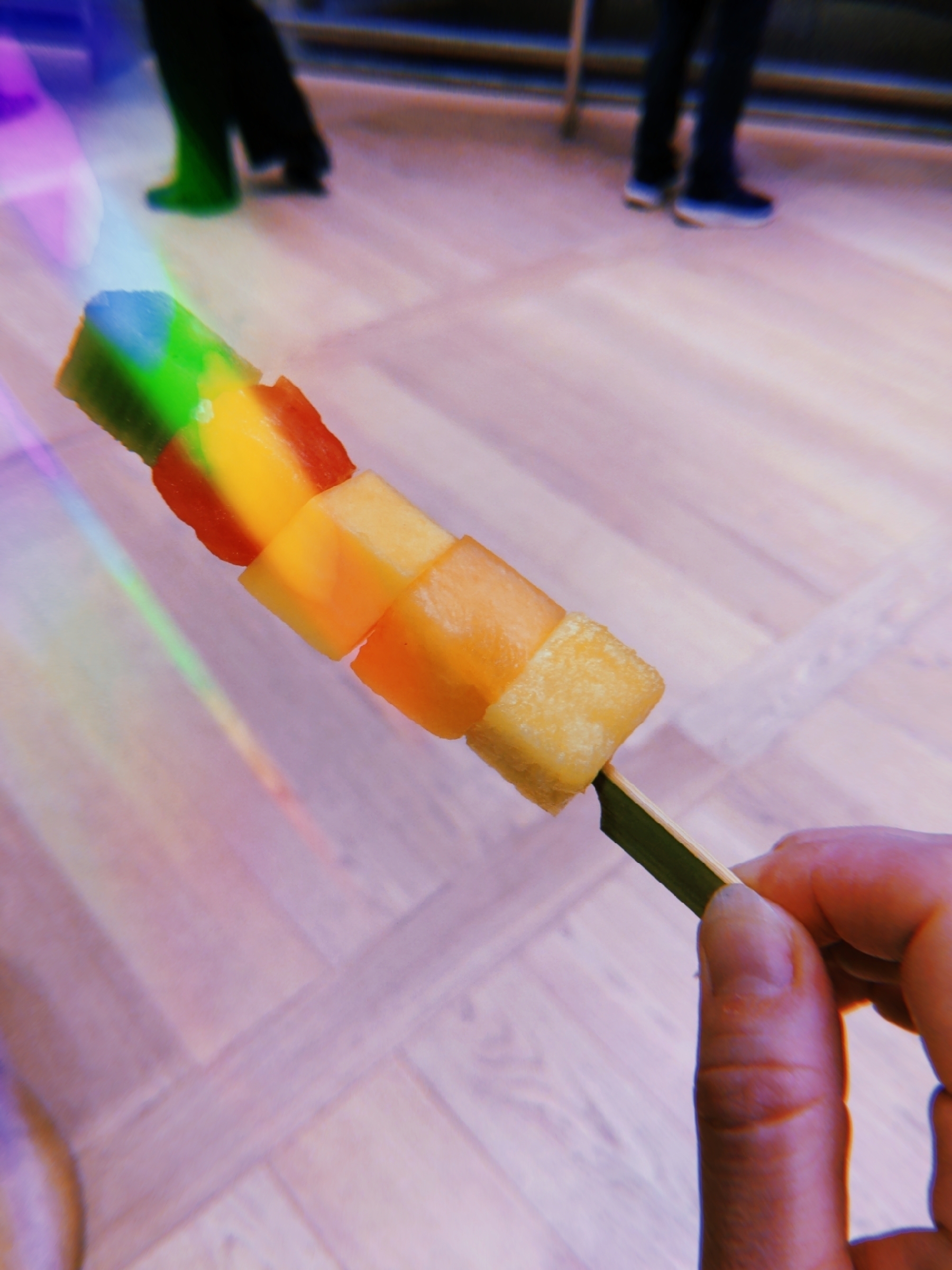 A hand is holding a skewer with colorful fruit pieces arranged in a gradient.