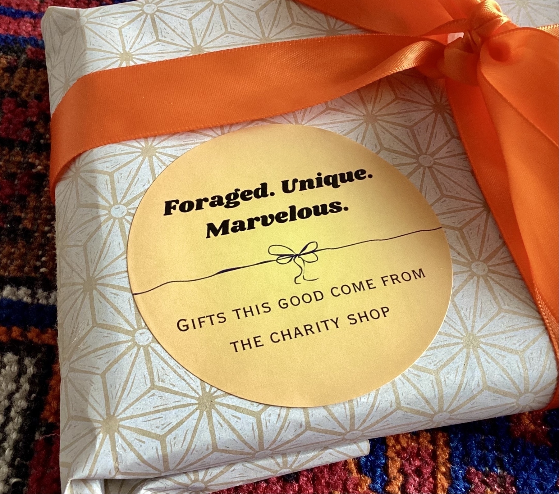 A wrapped gift with an orange ribbon features a sticker reading, "Foraged. Unique. Marvelous." indicating it comes from a charity shop.