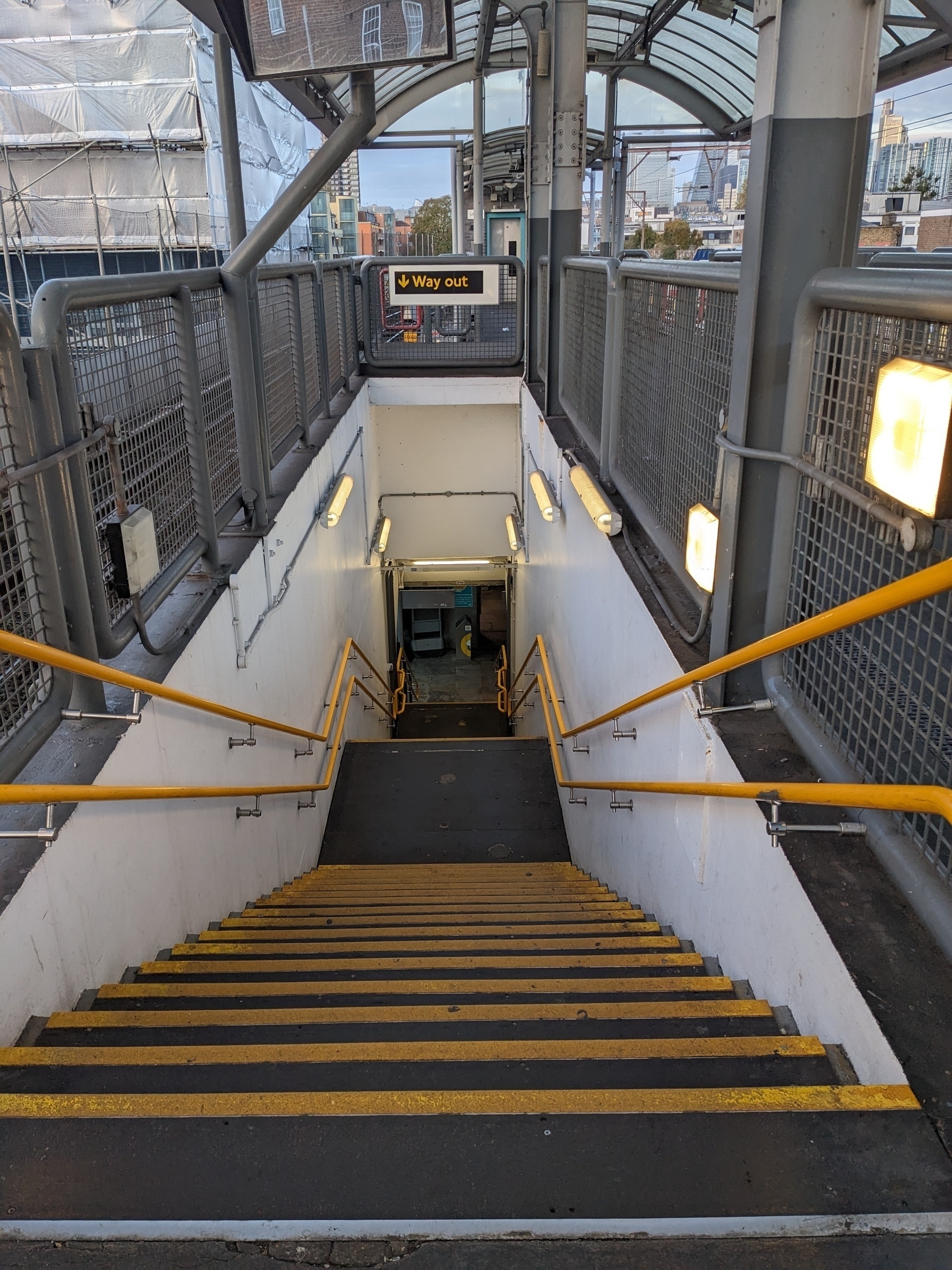 A stairway with yellow railings and steps leads down to a hallway marked with a "Way Out" exit sign at the top.