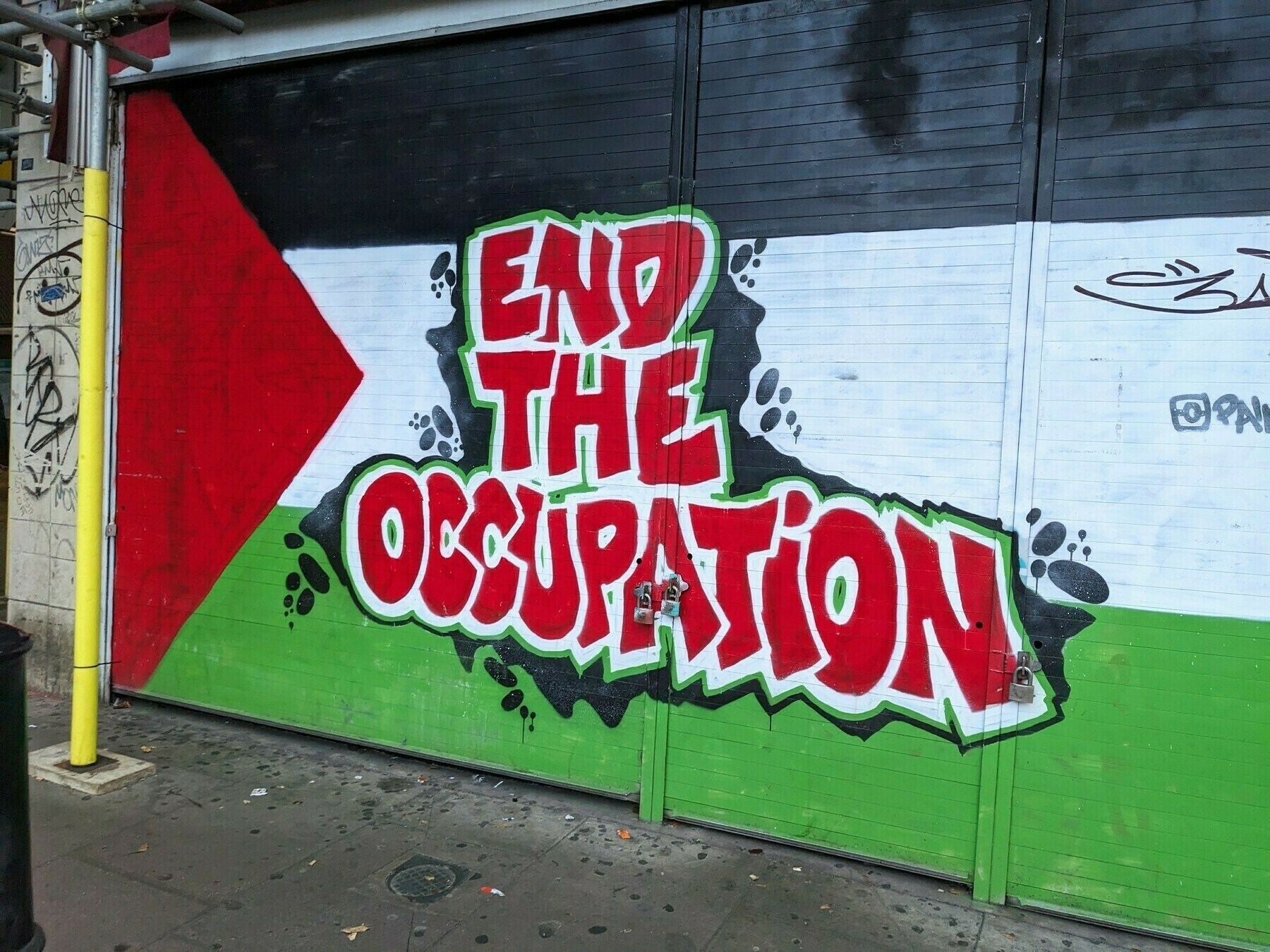 Graffiti art on a wall displays the words "END THE OCCUPATION" against a background of the Palestinian flag.