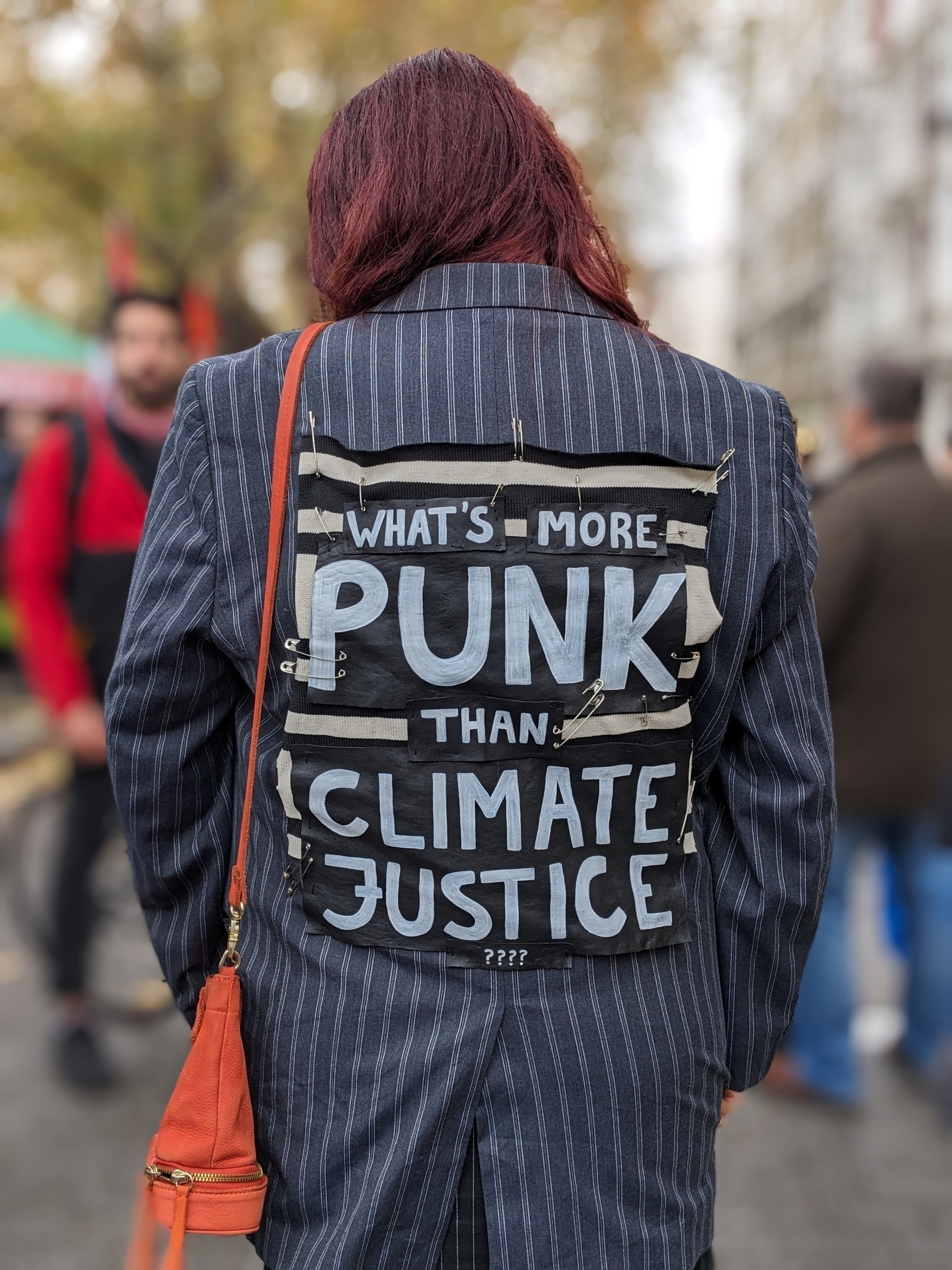 A person in the street, photo shows the back of their jacket with a home-made panel which says What's more punk than climate justice?