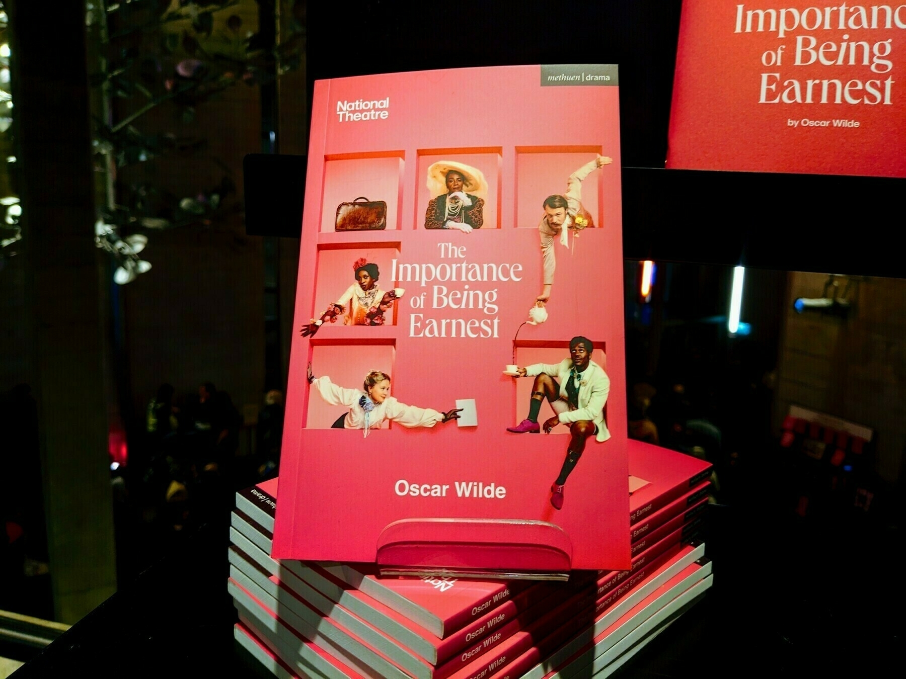 A stack of pink programmes for Oscar Wilde's "The Importance of Being Earnest" is displayed with cast photos on the cover.